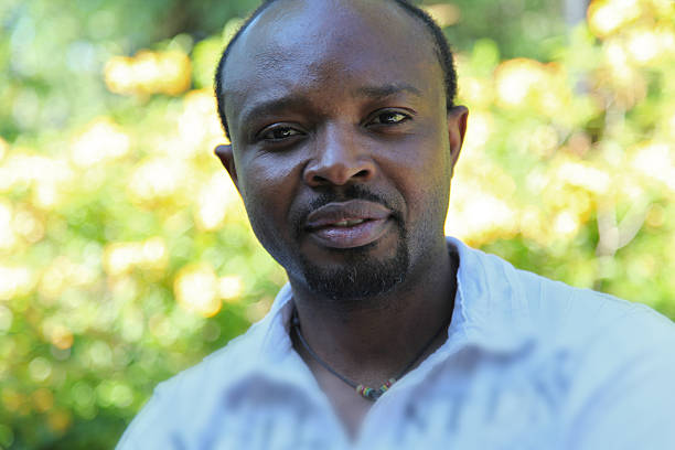 Young african man, looking positiv into the camera, wearing shirt, outdoors in a green environement